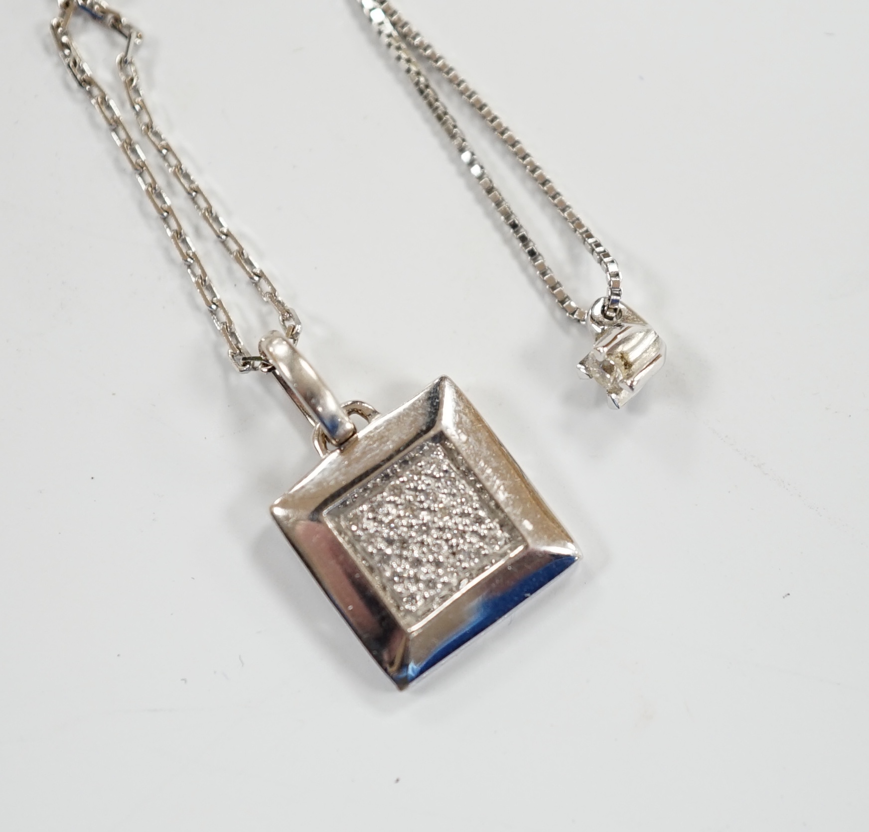 A modern Italian 18k white metal and diamond chip set pendant, on an 18k chain, 42cm and a white metal and diamond chip set square cluster pendant on an 18k chain, gross weight 6 grams.